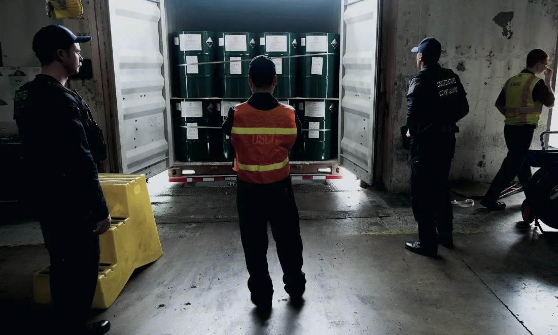 Inspectors standing at the open doors of a shipping container.