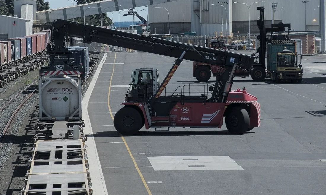 A reach stacker lifting a container onto a truck in a port yard.